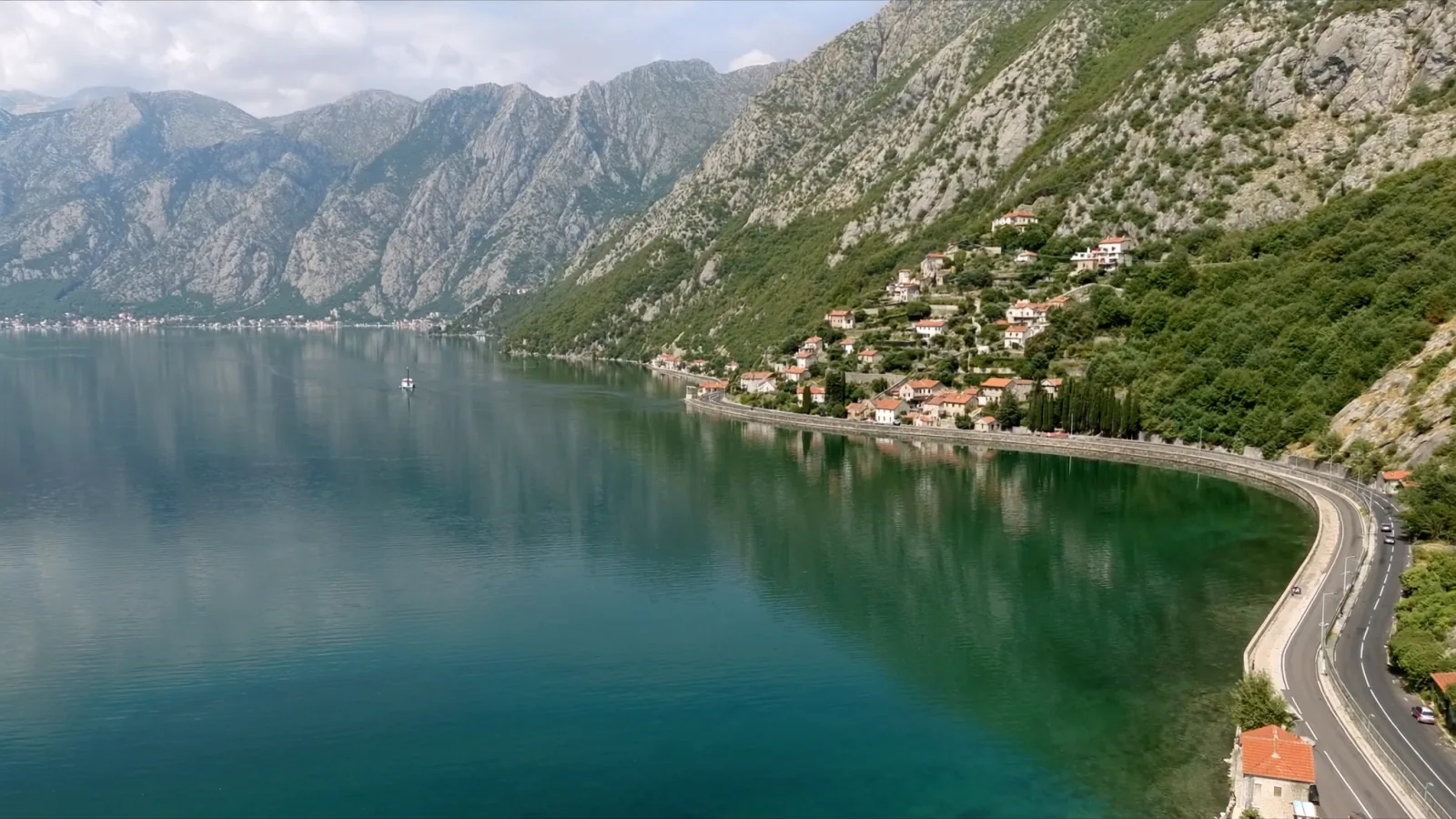 The M-1 coast road curving along the shore of the Bay of Kotor below steep grey mountains