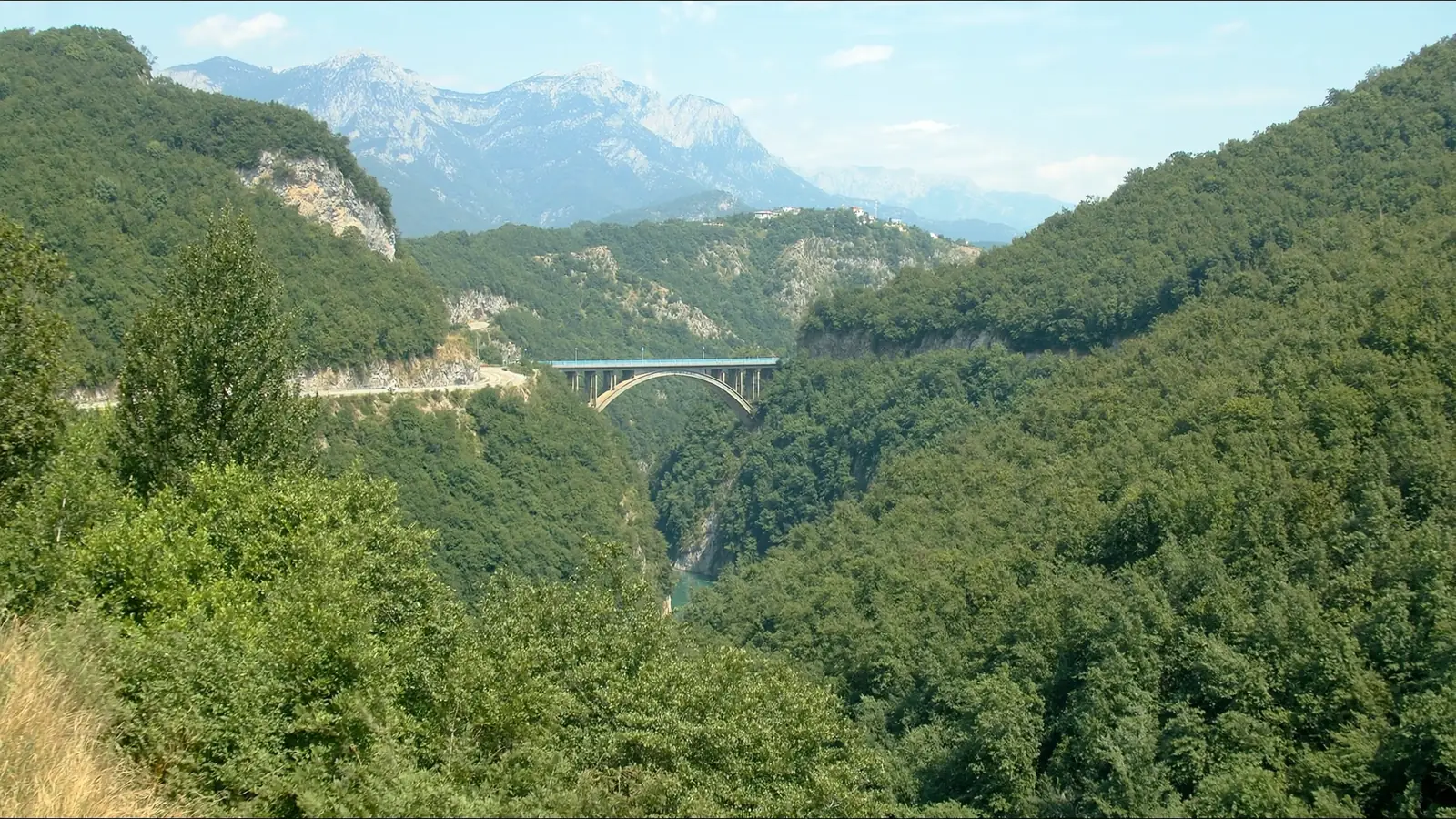 The old road through a wooded Montenegrin canyon, crossing on a concrete arch bridge