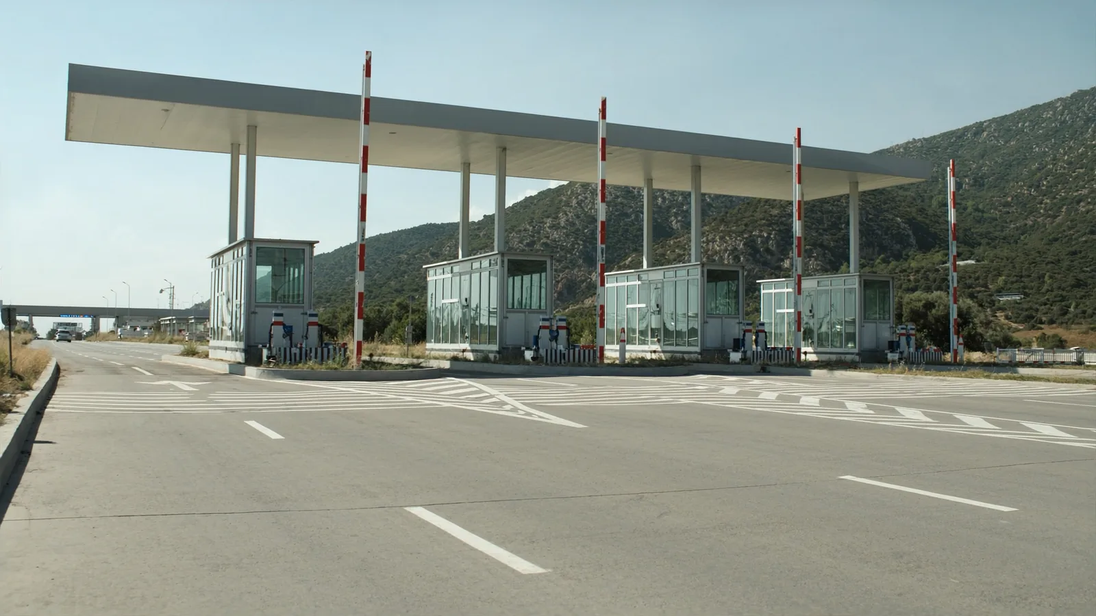 Toll lanes with raised barrier arms under an overhead canopy on a road through dry mountains